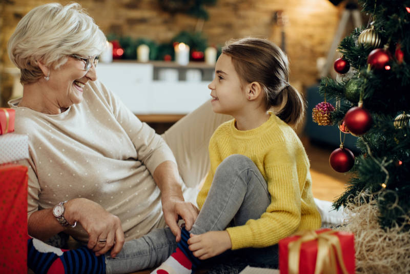Happy senior woman and her granddaughter talking while relaxing at home on Christmas. Family Impact - Alifts LLC